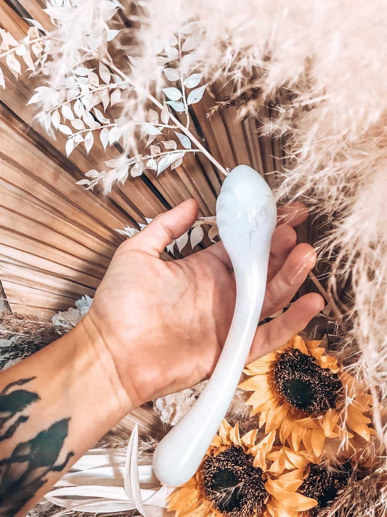 White glass pleasure wand with egg shaped tip. Pictured in models hand on background of sunflowers and pampas.
