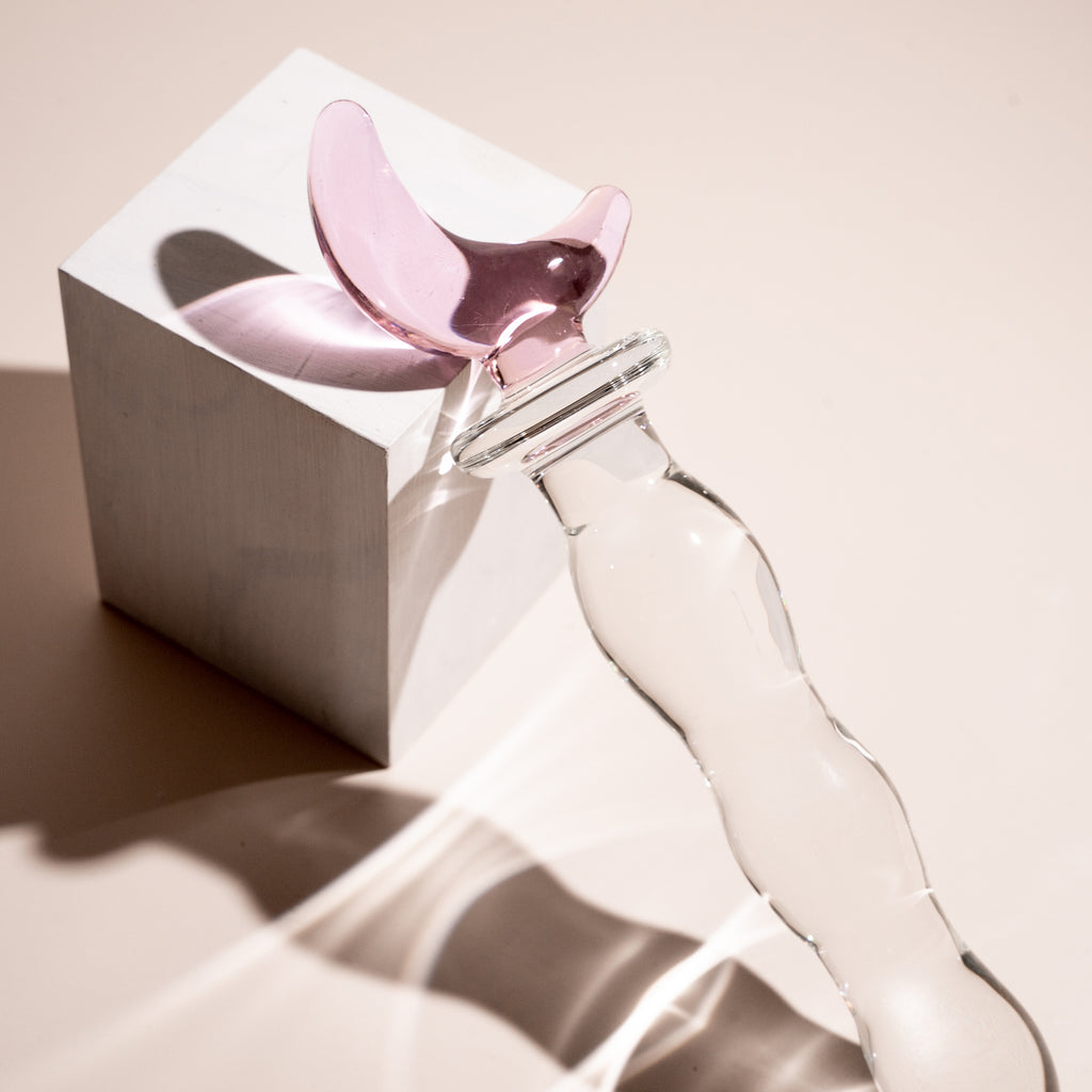 Rippled clear glass pleasure wand with pink moon handle. Pictured on beige background with a white block.
