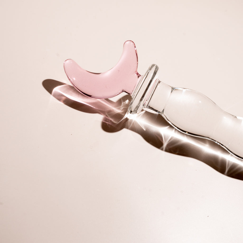 Rippled clear glass pleasure wand with pink moon handle. Pictured on beige background.