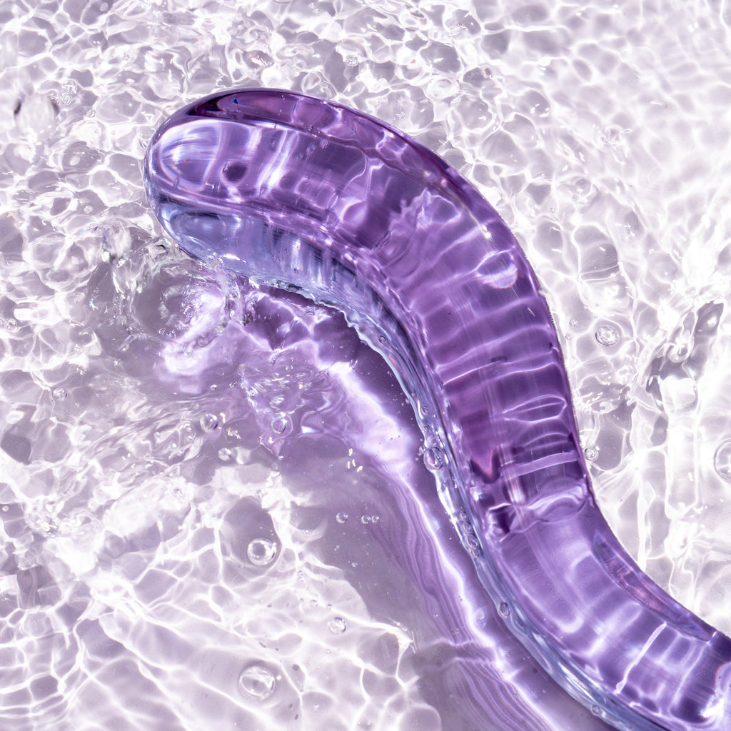 Pussy paddle thick curved pleasure wand in lilac. Pictured on background of water.